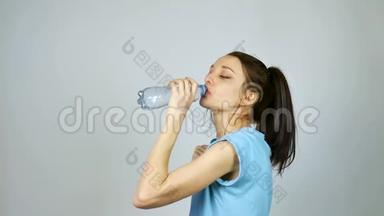 一个长着深色头发的布鲁内特女孩在灰色的环境下锻炼后，正在用塑料透明瓶子喝纯<strong>净水</strong>